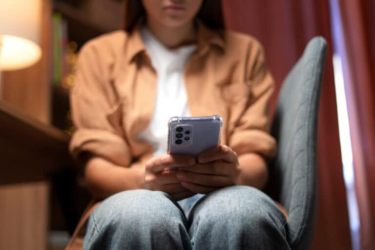 woman holding phone while sitting on desk chair.